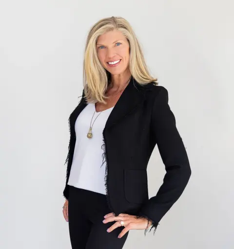 Amy Nakos smiling in a black blazer against a light studio background