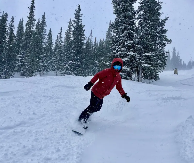 Jennifer Luberto snowboarding through fresh powder among evergreens