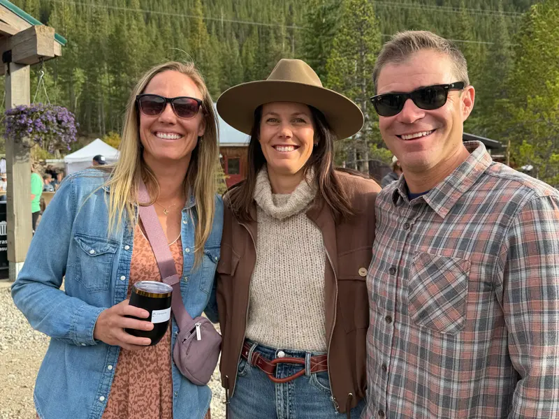 Three people posing outdoors in front of a forest, each wearing sunglasses and smiling.