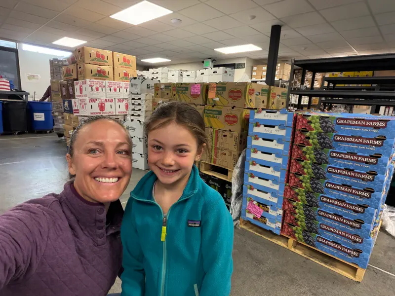 A woman and a young girl taking a selfie in a warehouse filled with stacks of produce boxes.